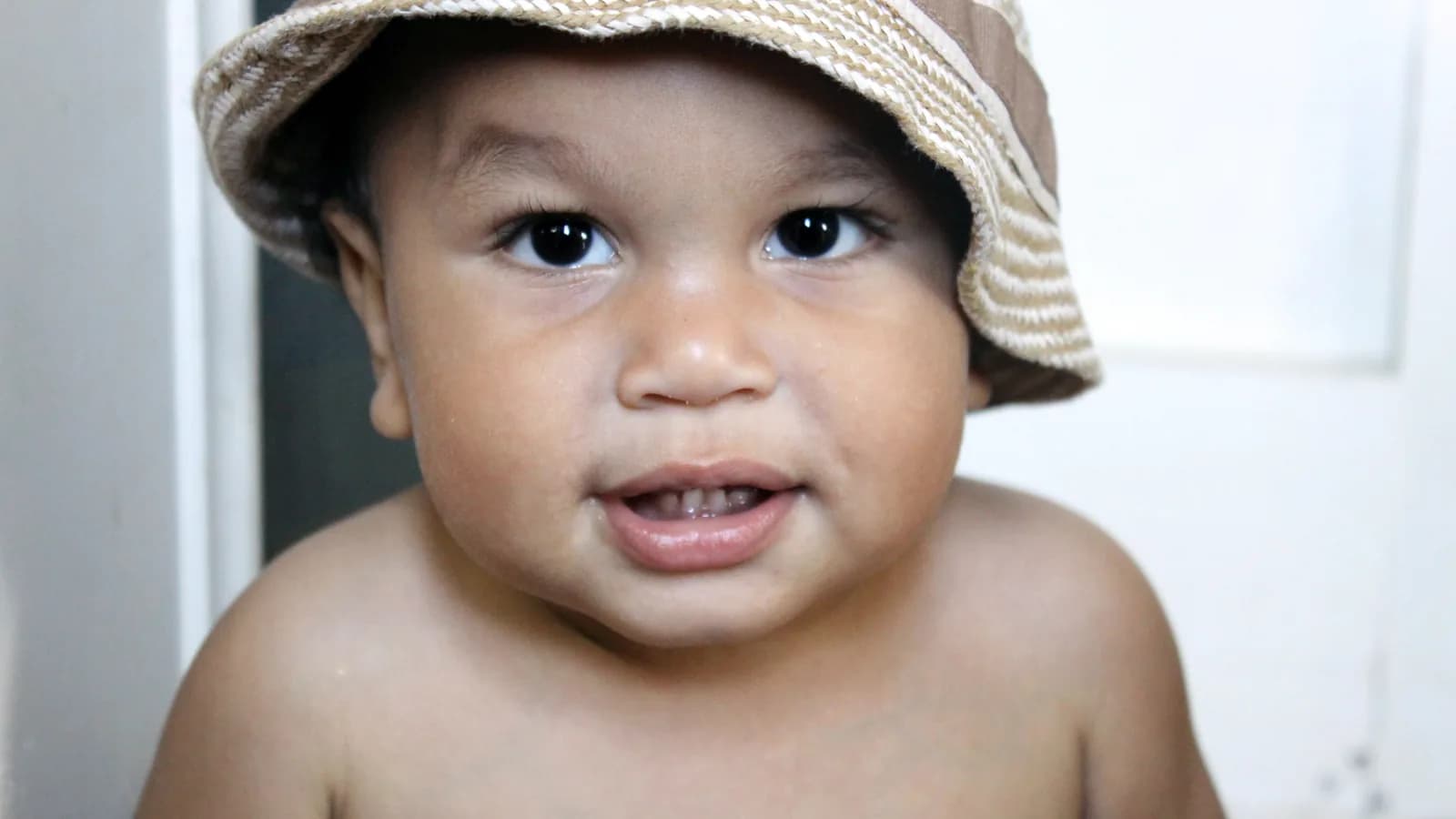 Niño pequeño sonriendo en primer plano, con un gorro de tela y el fondo desenfocado