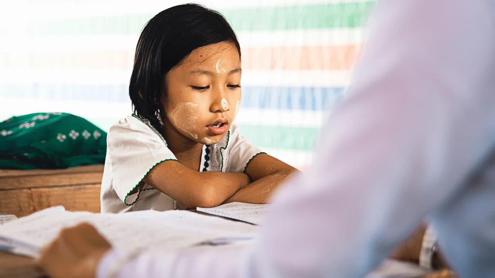 Niña apoyada en la mesa mientras una persona adulta le señala algo en el cuaderno