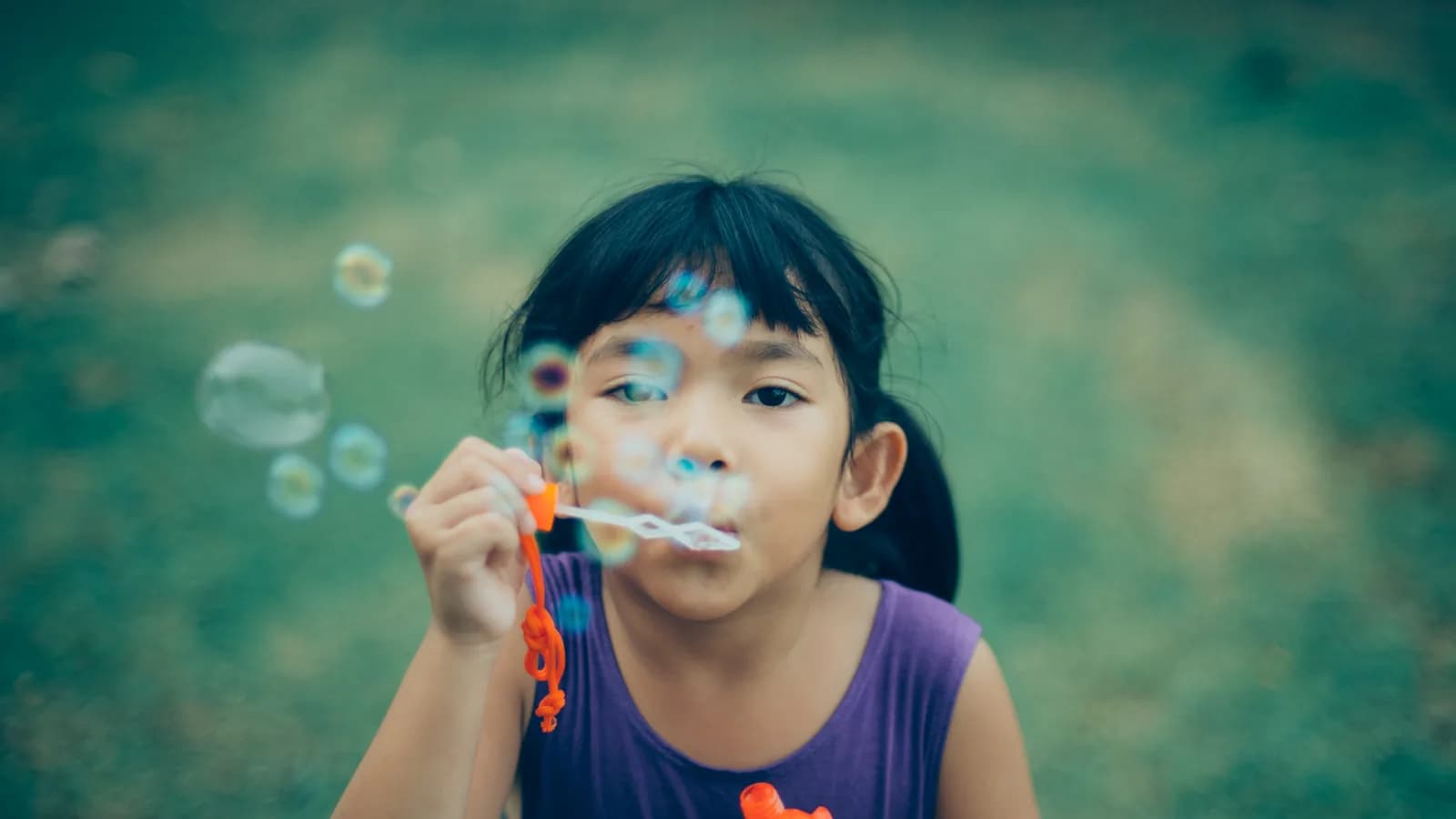 Niña soplando para hacer pompas de jabón, en primer plano sobre un fondo verde