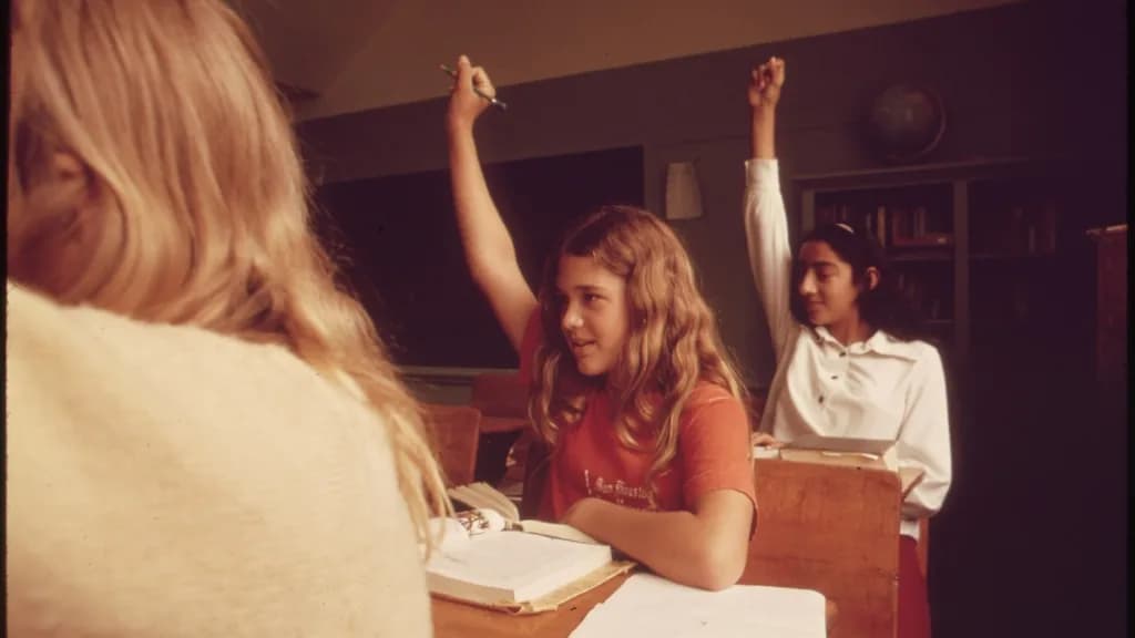 Varias alumnas levantan la mano en clase, sentadas en sus pupitres