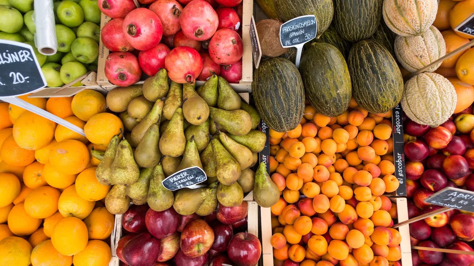Puesto de mercado con naranjas, manzanas, peras y melones ordenados por cajas