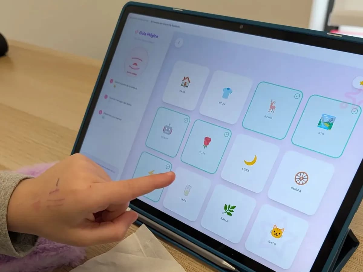 Niña señalando una actividad de SandiApp en una tablet durante la sesión de logopedia
