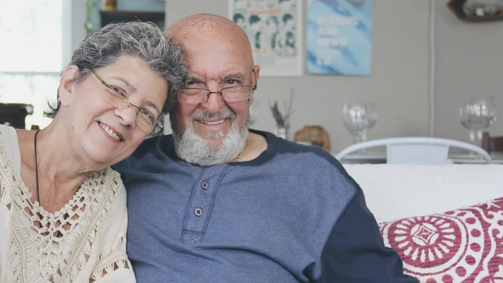 Pareja mayor sonriendo, abrazada, en el salón de su casa